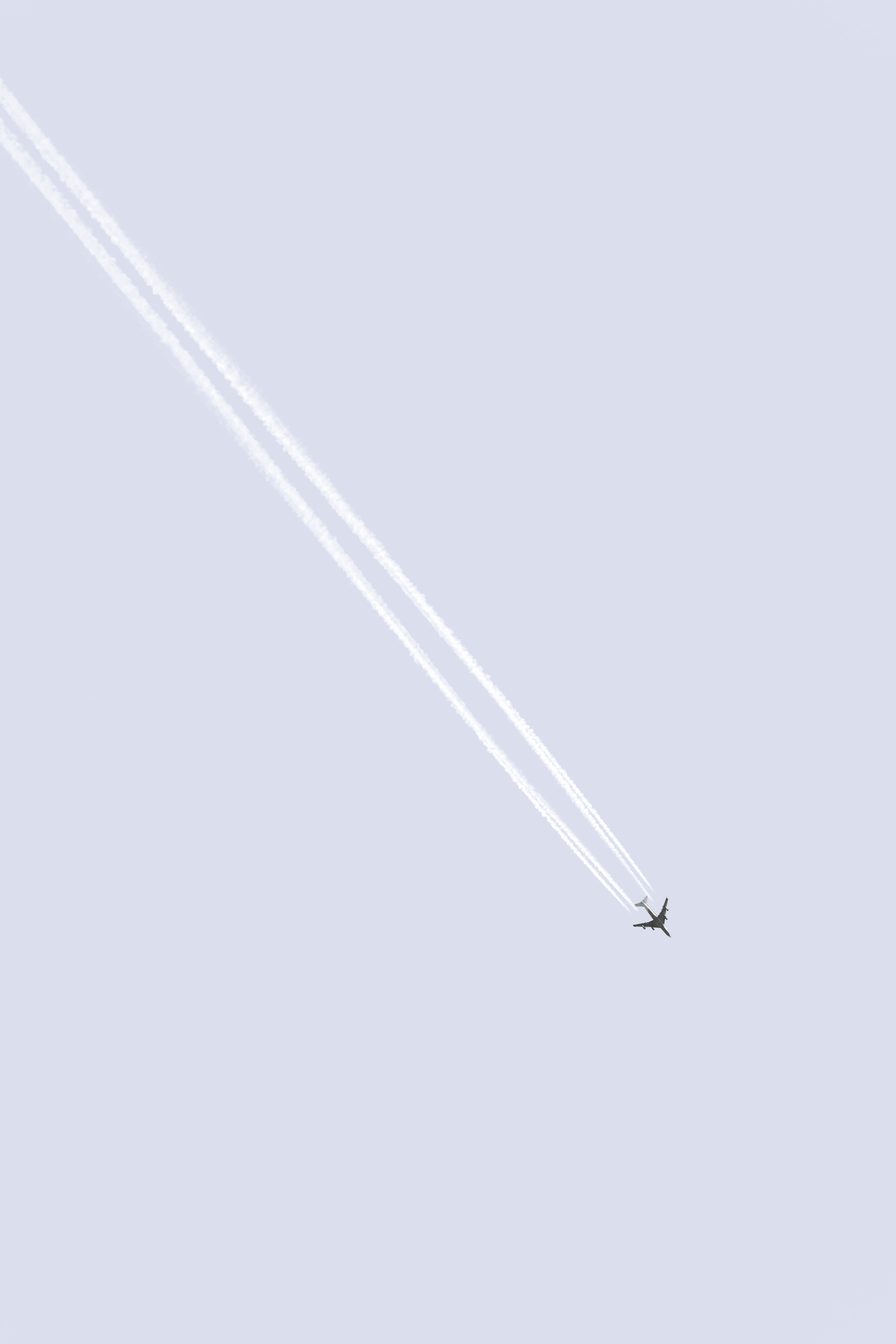 View from the ground of an aeroplane flying overhead. The sky is a pale red-blue colour and the aeroplane leaves contrails behind it.